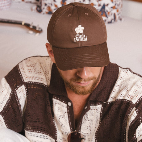 A man wearing a brown cap with 'Club Pantai' 
