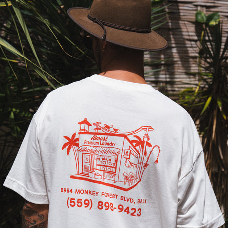 A person wearing a white Club Pantai t-shirt with Laundry Shop printed on it.