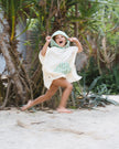 Child in a Club Pantai white poncho with green text running outdoors in a natural setting