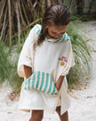 A child wrapped in a Club Pantai towel with a striped pattern on a beach