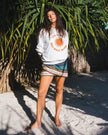 A woman wearing a 'Club Pantai Bali Beach' t-shirt standing under palm trees on a sandy beach.