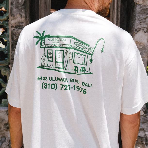 Person wearing a white t-shirt with Club Pantai Shop green graphics.